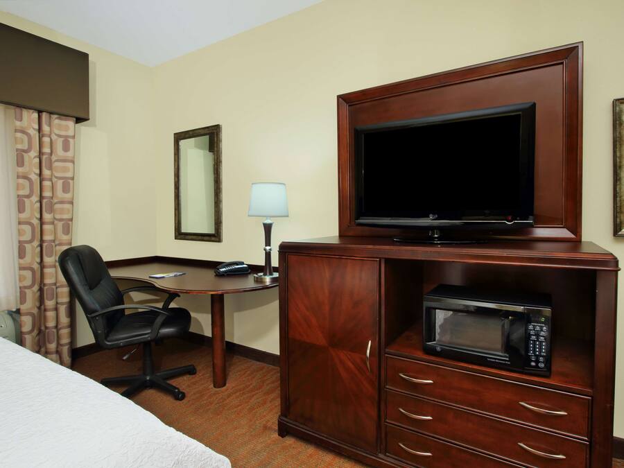 A hotel room with a bed, a desk, a chair, a television on a wooden cabinet, and a microwave.