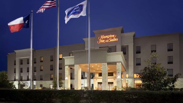 Ein Hotel mit einem Schild, auf dem 'Hampton Inn & Suites' steht, und mit den Flaggen der USA und von Texas.