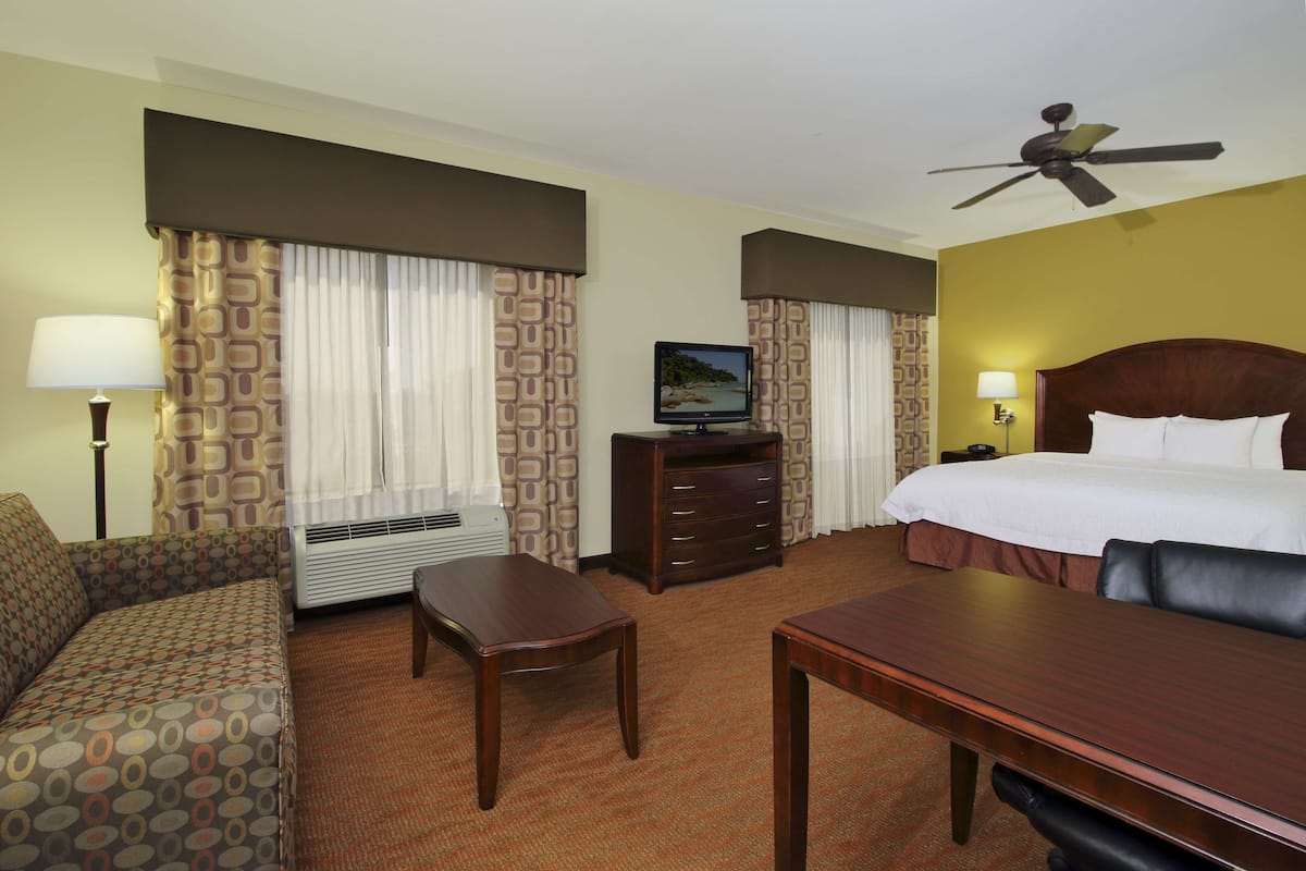 Quarto de hotel com cama, escrivaninha, cadeira, televisão, aquecedor e cortinas.