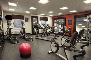 Un gimnasio con cintas de correr, máquinas elípticas y una pelota de ejercicios roja.