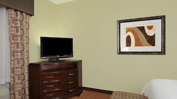 Habitación de hotel con una televisión de pantalla plana sobre una cómoda de madera, un cuadro abstracto enmarcado en la pared y una colcha estampada.