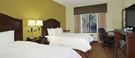 A hotel room with two beds, a desk, a chair, a TV, and a window with curtains.