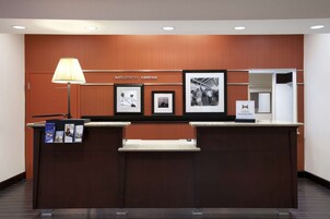 Un mostrador de recepción con un cartel que dice "welcome to conroe", fotografías enmarcadas y un letrero de "Hilton Honors".