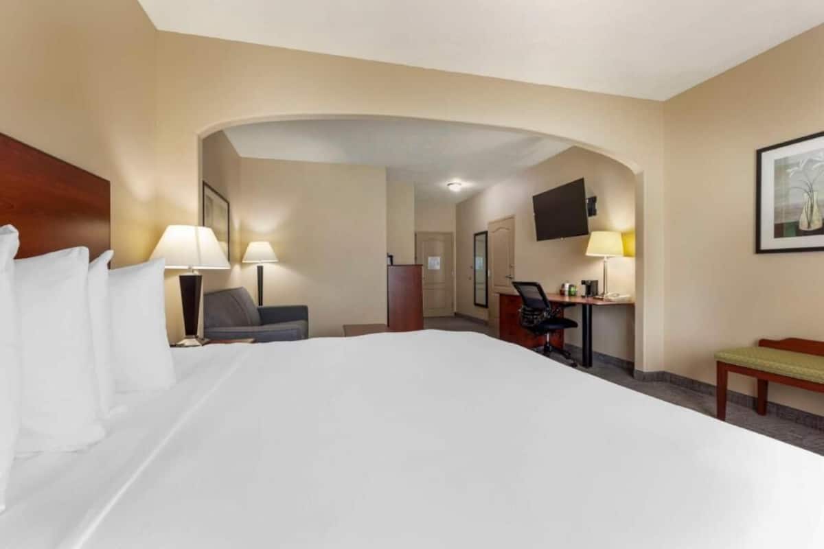 Une chambre d’hôtel avec un grand lit, un bureau, une chaise, une lampe, un téléviseur et un tableau encadré au mur.
