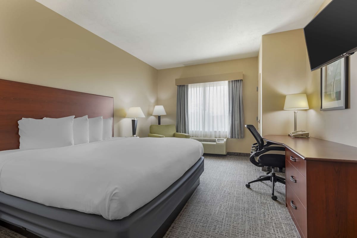 Une chambre d’hôtel avec un grand lit, un bureau, une chaise, un téléviseur à écran plat et une fenêtre avec des rideaux.