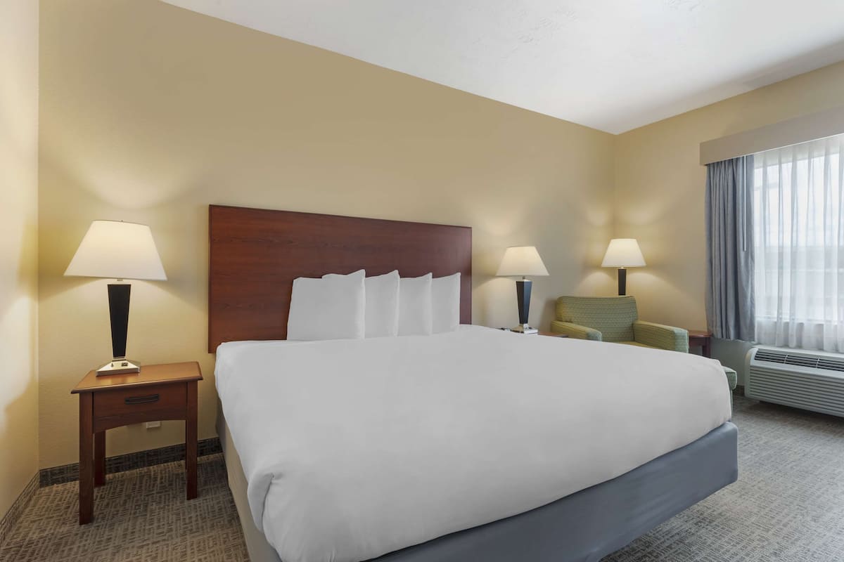 Une chambre d’hôtel avec un grand lit, deux tables de chevet avec des lampes, une chaise et une fenêtre avec des rideaux.