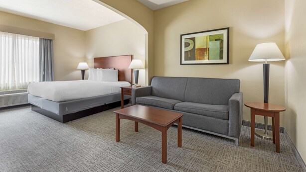 Een hotelkamer met een bed, een grijze bank, een klein houten tafeltje en twee bedlampen.