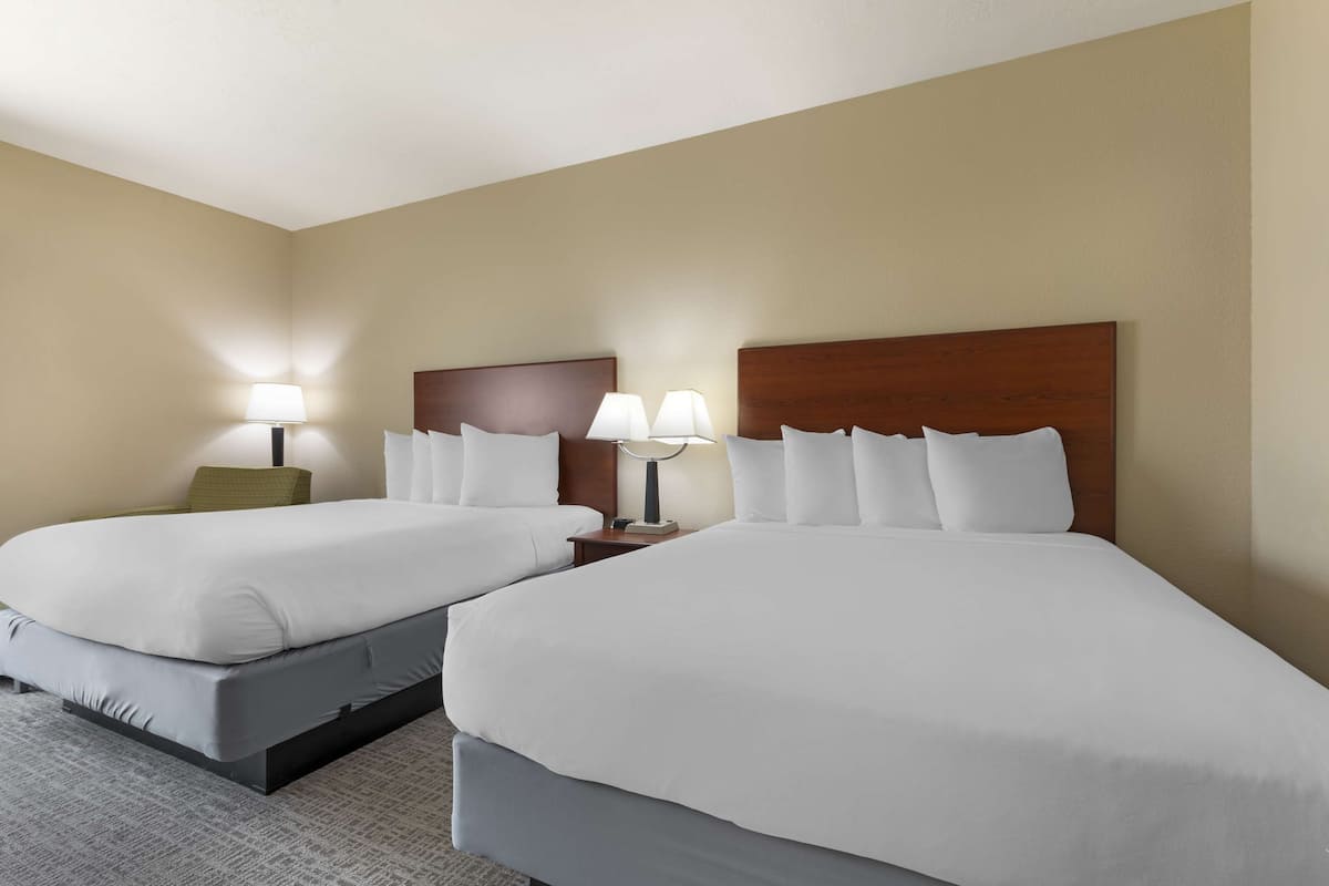 Une chambre d’hôtel avec deux lits, chacun doté de draps blancs et d’une tête de lit en bois. Il y a deux tables de chevet avec des lampes.
