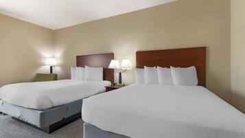 A hotel room with two beds, each with white linens and a wooden headboard. There are two bedside tables with lamps.