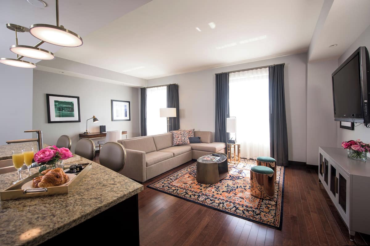 Ein modernes Wohnzimmer mit Sofa, Couchtisch und Fernseher. Es gibt einen Essbereich mit Tisch und Stühlen sowie eine Küchenzeile mit Spüle und Arbeitsfläche.