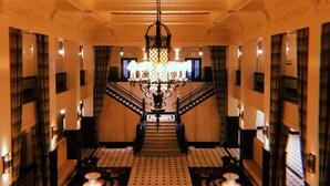 A grand staircase with a chandelier, flanked by patterned walls and curtains, leading to an upper floor. - The Mayo Hotel (Tulsa)