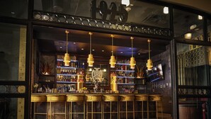 A bar with multiple hanging lights, shelves with bottles, and a large number above the entrance. - The Mayo Hotel (Tulsa)