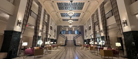 A grand lobby with a checkered floor, a central staircase, and chandeliers.
