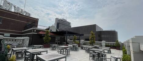 An outdoor patio area with multiple tables and chairs, a brick building, and a modern glass building in the background.