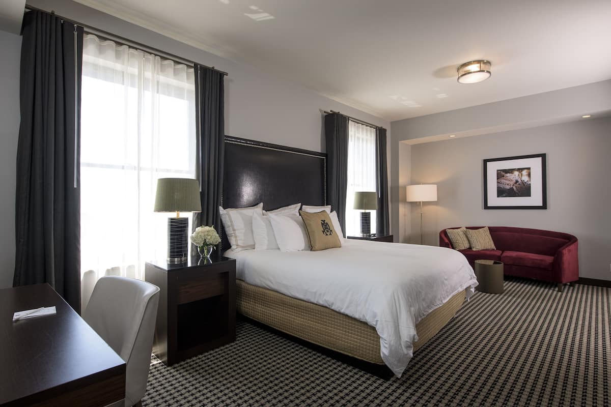 Ein Hotelzimmer mit einem großen Bett, einem Schreibtisch, einem Sessel, einer roten Couch und einem gerahmten Bild an der Wand.