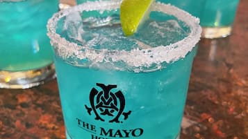 Ein Glas blauer Cocktail mit Limettenscheibe und gesalzenem Rand, beschriftet mit 'The Mayo Hotel'.
