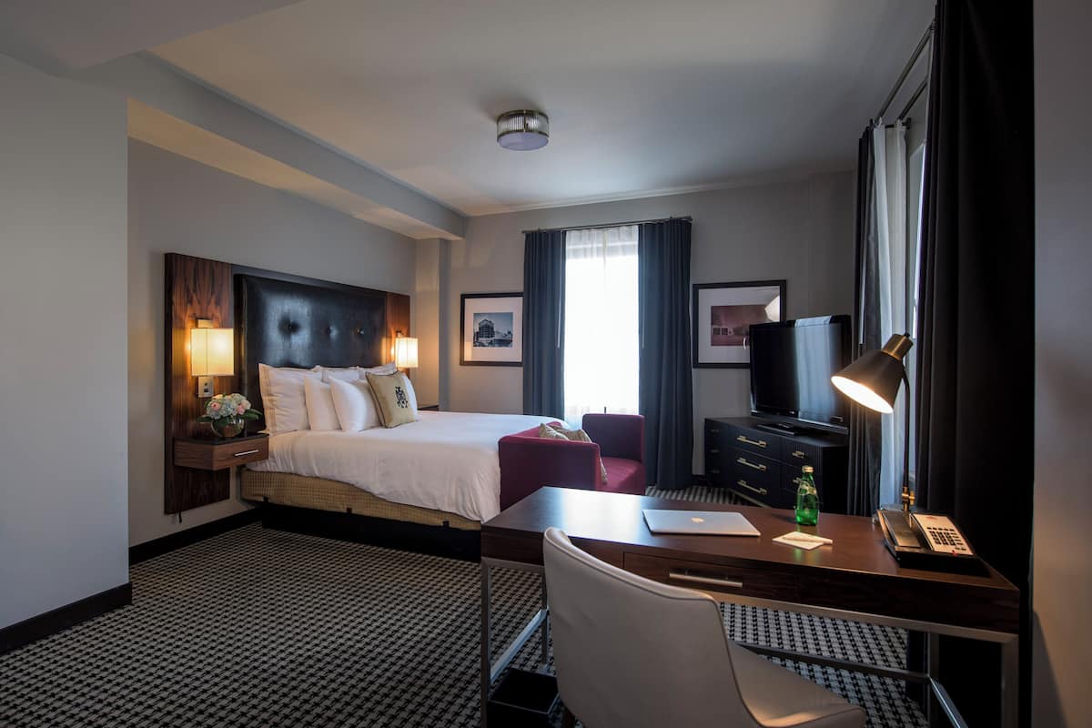Ein Hotelzimmer mit einem großen Bett, einem Schreibtisch mit Stuhl, einem Fernseher und einer Lampe.