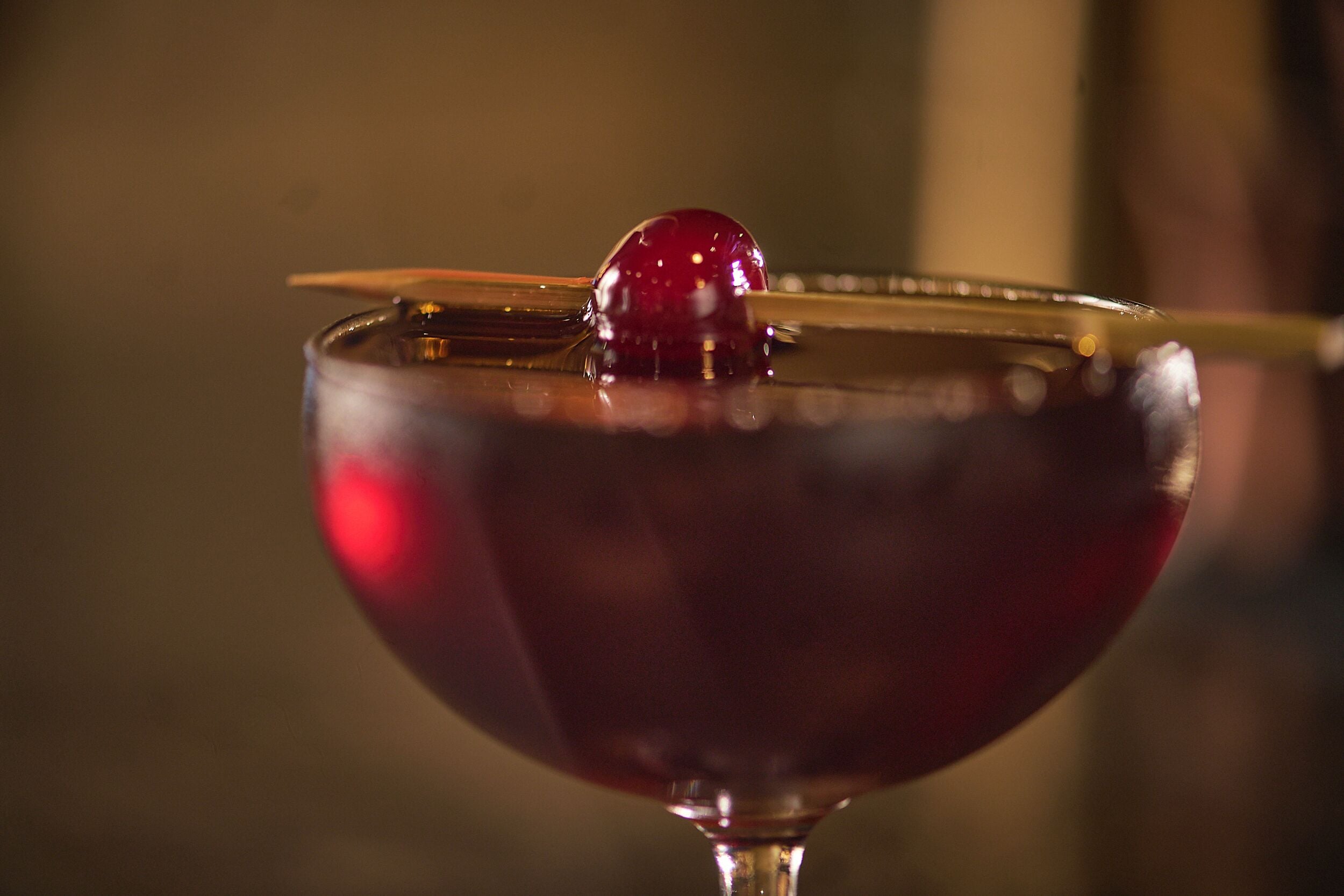 A close-up of a cocktail glass with a cherry on a cocktail stick.