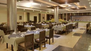 A spacious dining area with multiple tables and chairs, large pillars, and a well-lit ceiling with recessed lighting. - Inder Residency Resort & Spa Udaipur (Udaipur)