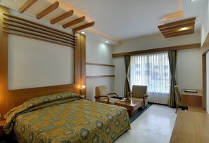 A hotel room with a bed, two chairs, a desk, and a large window with curtains. - Inder Residency Resort & Spa Udaipur (Udaipur)