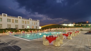 A poolside area with tables set for dining, a swimming pool, and a building in the background. - Inder Residency Resort & Spa Udaipur (Udaipur)