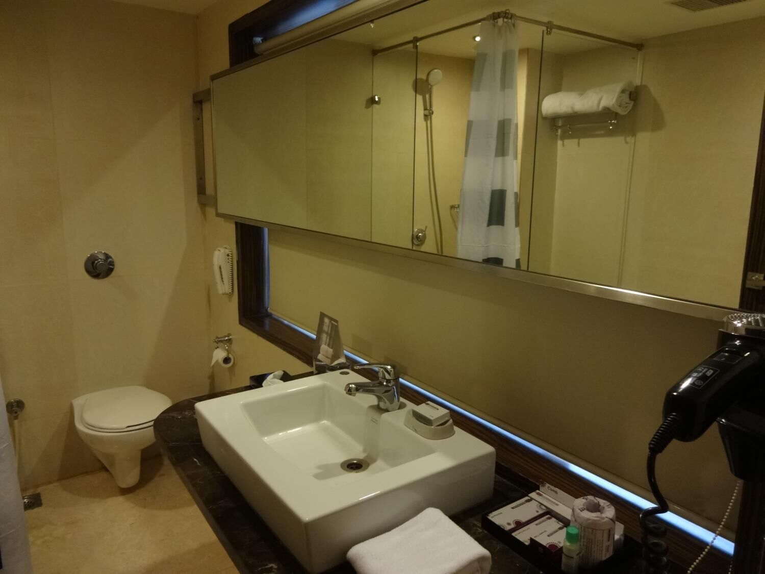 A bathroom with a toilet, a sink, a large mirror, and a hairdryer.