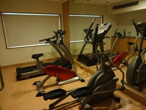 A gym with multiple stationary bikes and treadmills, wooden flooring, and large windows. - Minerva Grand Banjara Hills (Hyderabad)