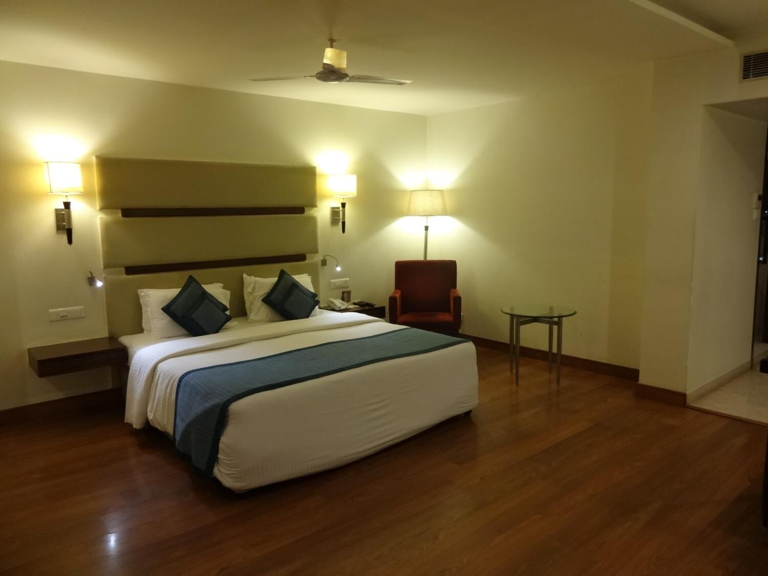 Une chambre d’hôtel avec un grand lit, une chaise, une petite table et deux lampes fixées au mur.
