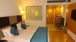 A hotel room with two beds, a TV, a bedside table with a remote control, and a bathroom visible through an open door. - Minerva Grand Banjara Hills (Hyderabad)