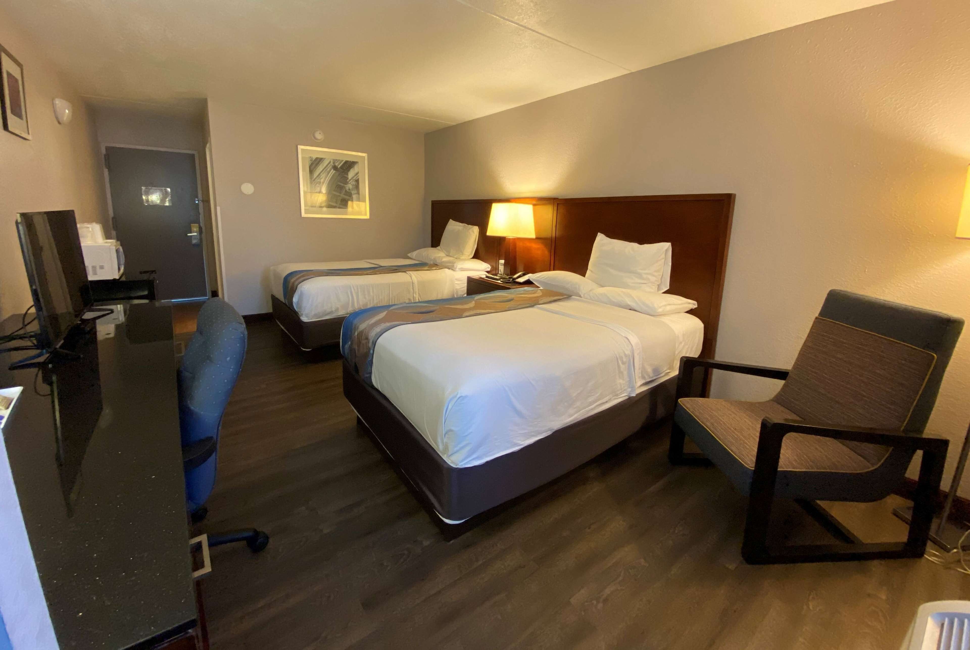 Habitación de hotel con dos camas, un escritorio, una silla y un televisor.