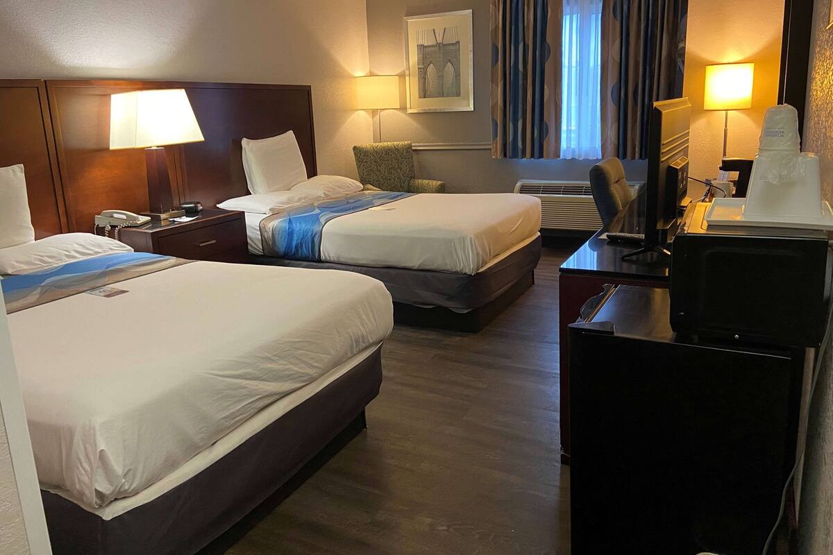 A hotel room with two beds, a desk with a computer, a phone, and a lamp.