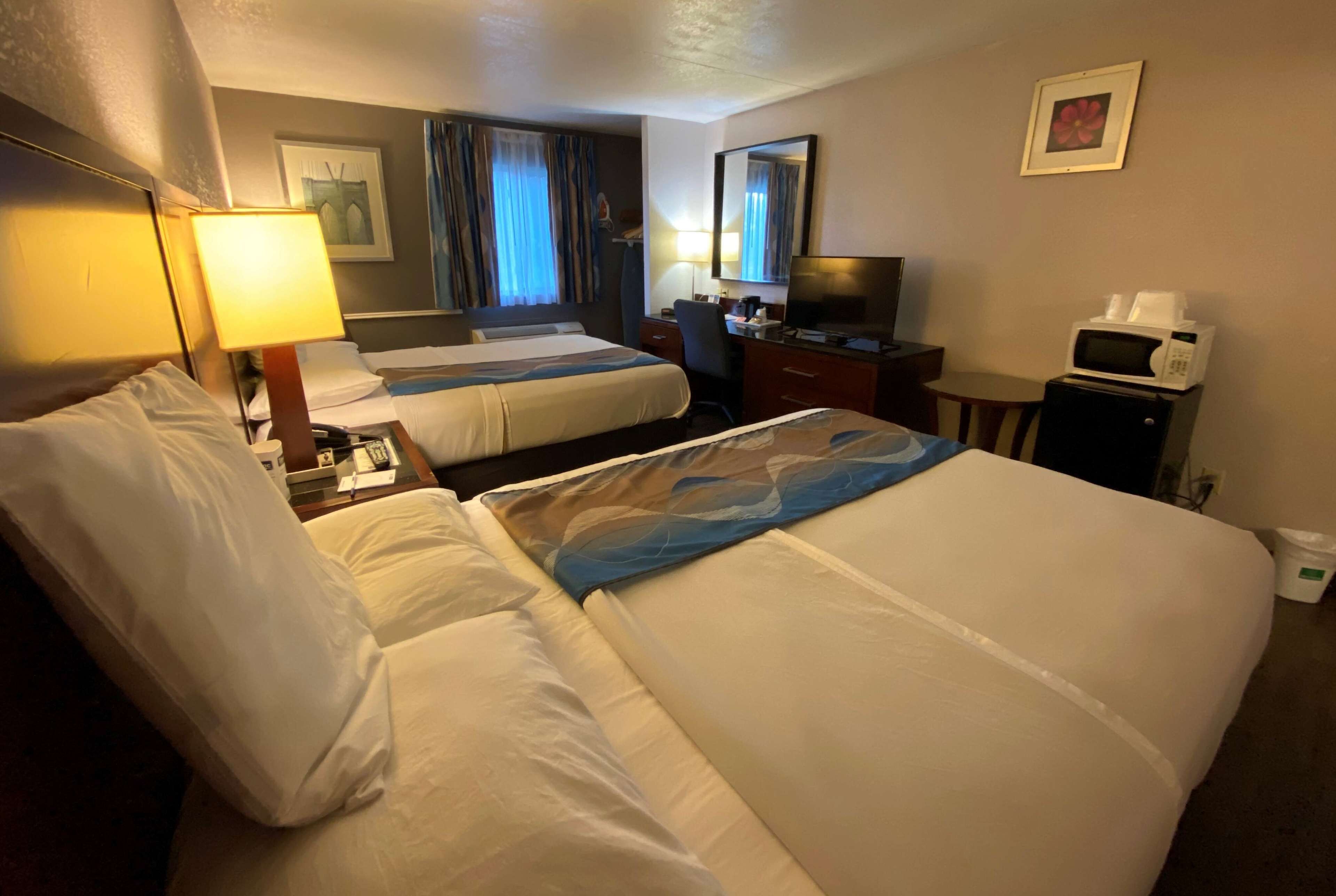 A hotel room with two beds, a desk with a computer, a microwave, and a TV.