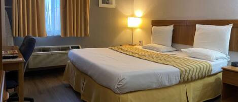 A hotel room with a bed, a desk, a chair, a lamp, and a window with curtains.