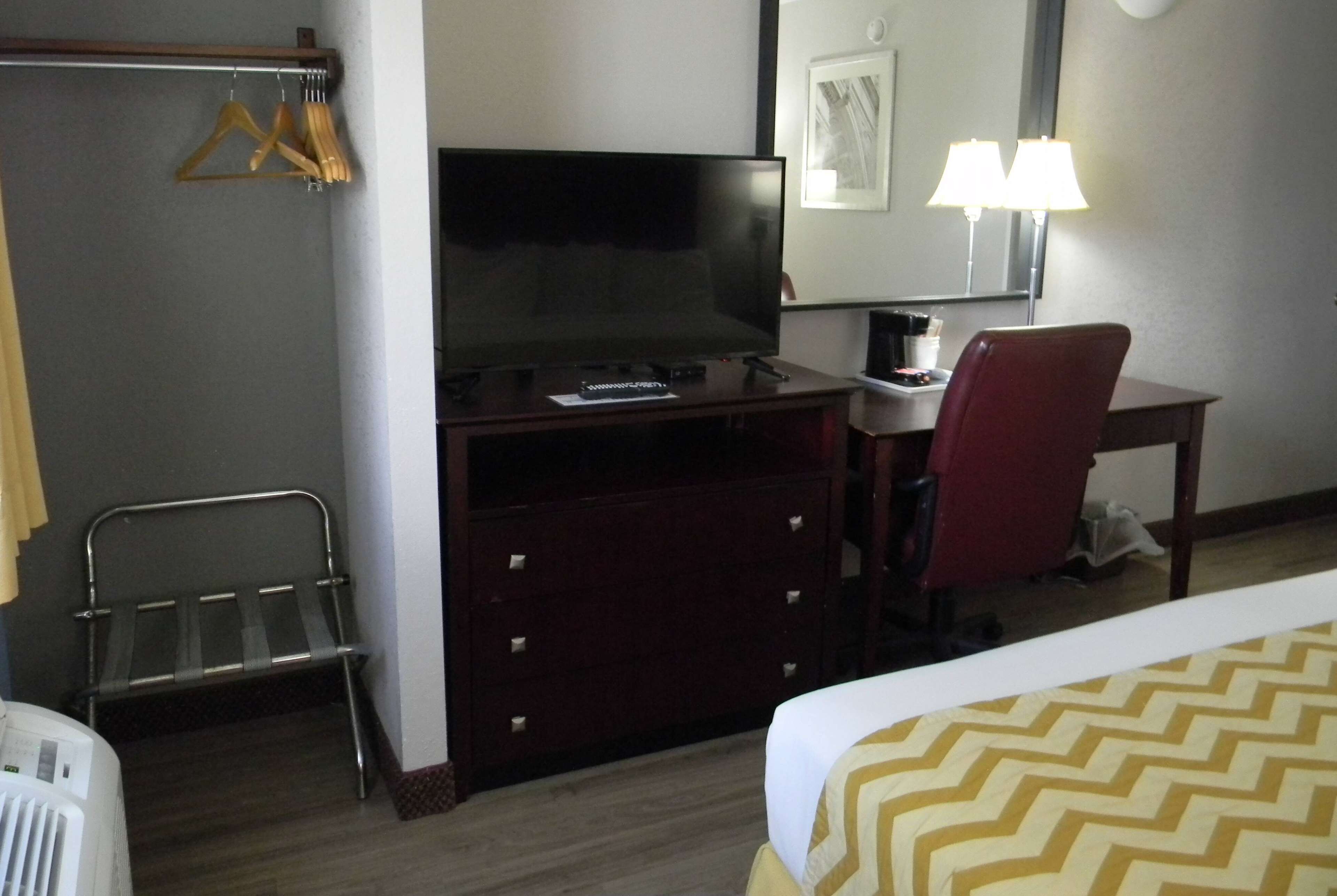 A hotel room with a bed, a desk with a chair, a television, a mirror, and a lamp.