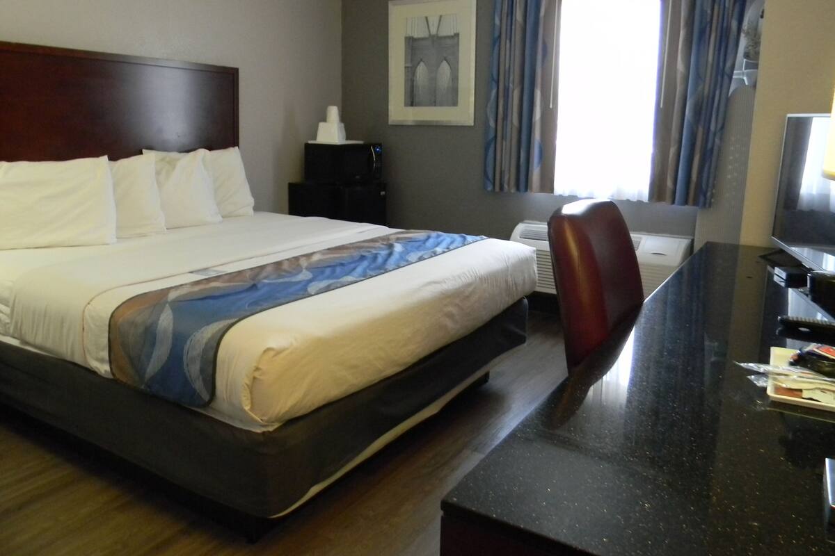 A hotel room with a bed, a desk, a chair, a television, and a window with curtains.