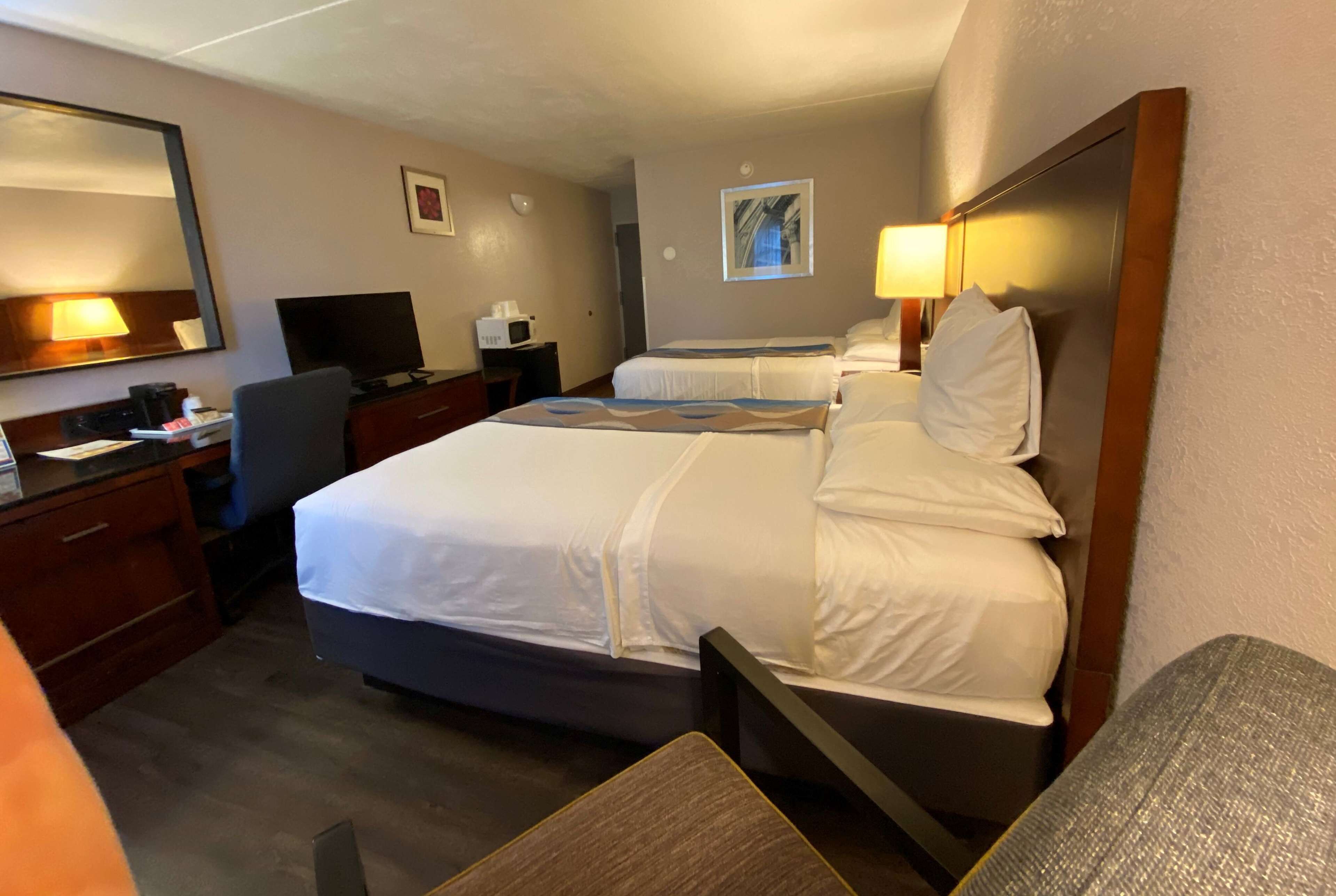 Una habitación de hotel con una cama grande, un escritorio con computadora, un televisor y un microondas.