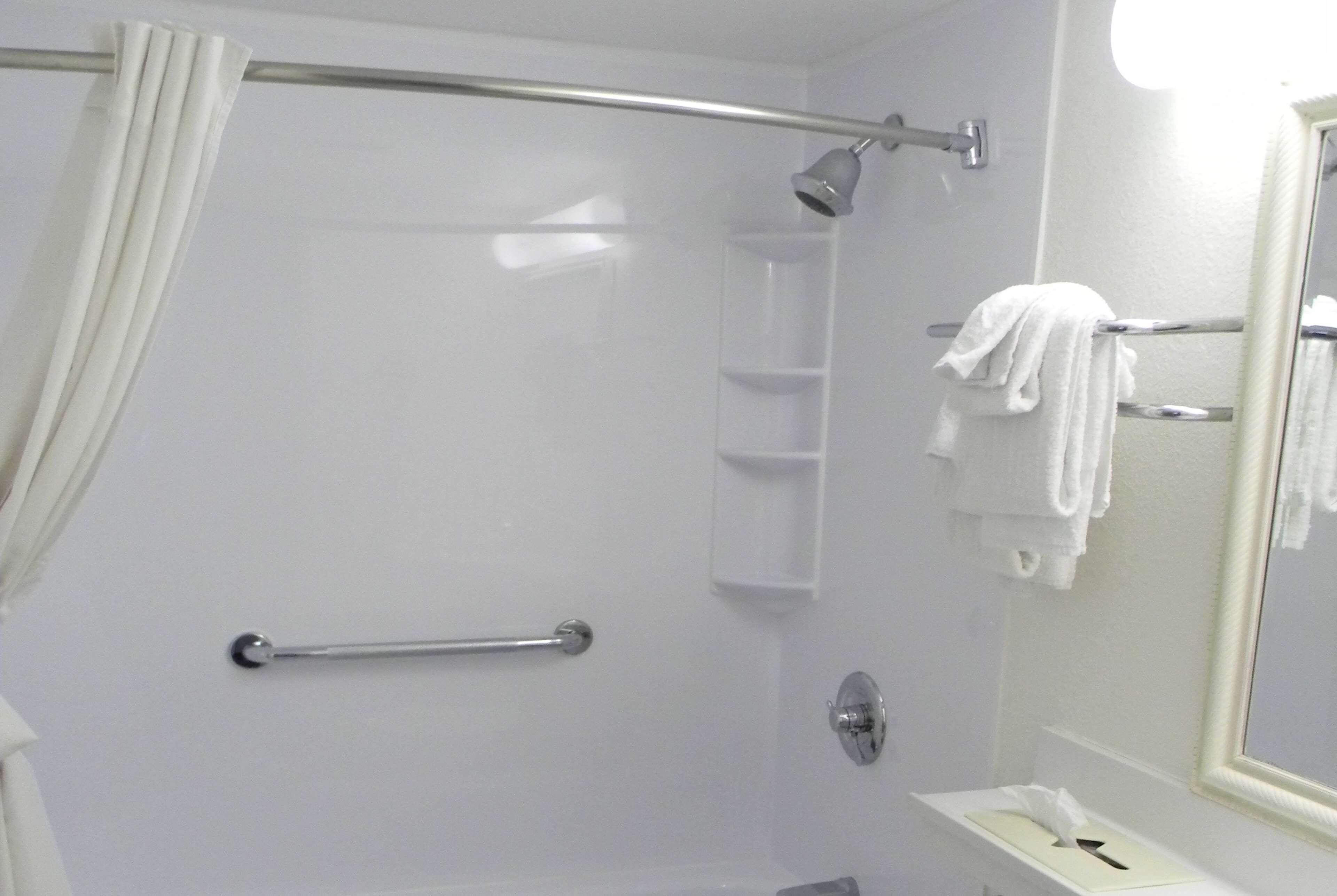 Un baño con ducha, toallero, espejo y estante.
