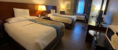 A hotel room with two beds, a desk, a chair, a microwave, and a window with curtains.