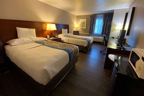 A hotel room with two beds, a desk, a chair, a microwave, and a window with curtains.