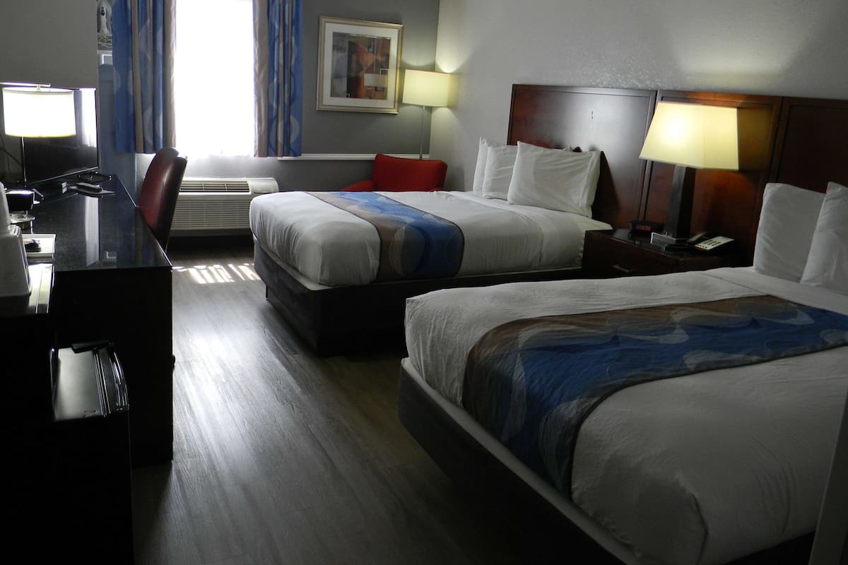 Une chambre d’hôtel avec deux lits, un bureau avec une chaise, une télévision et une lampe.