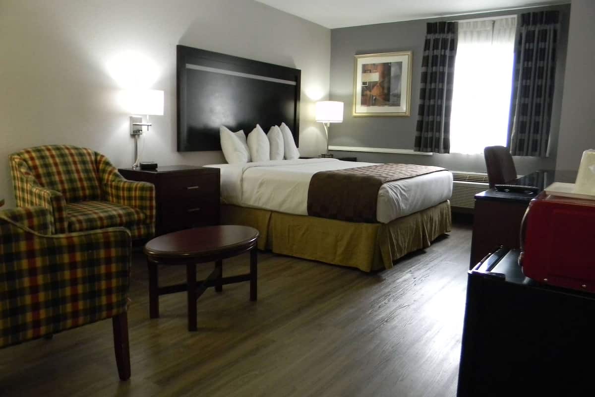 A hotel room with a bed, a chair, a small table, a desk, and a lamp.