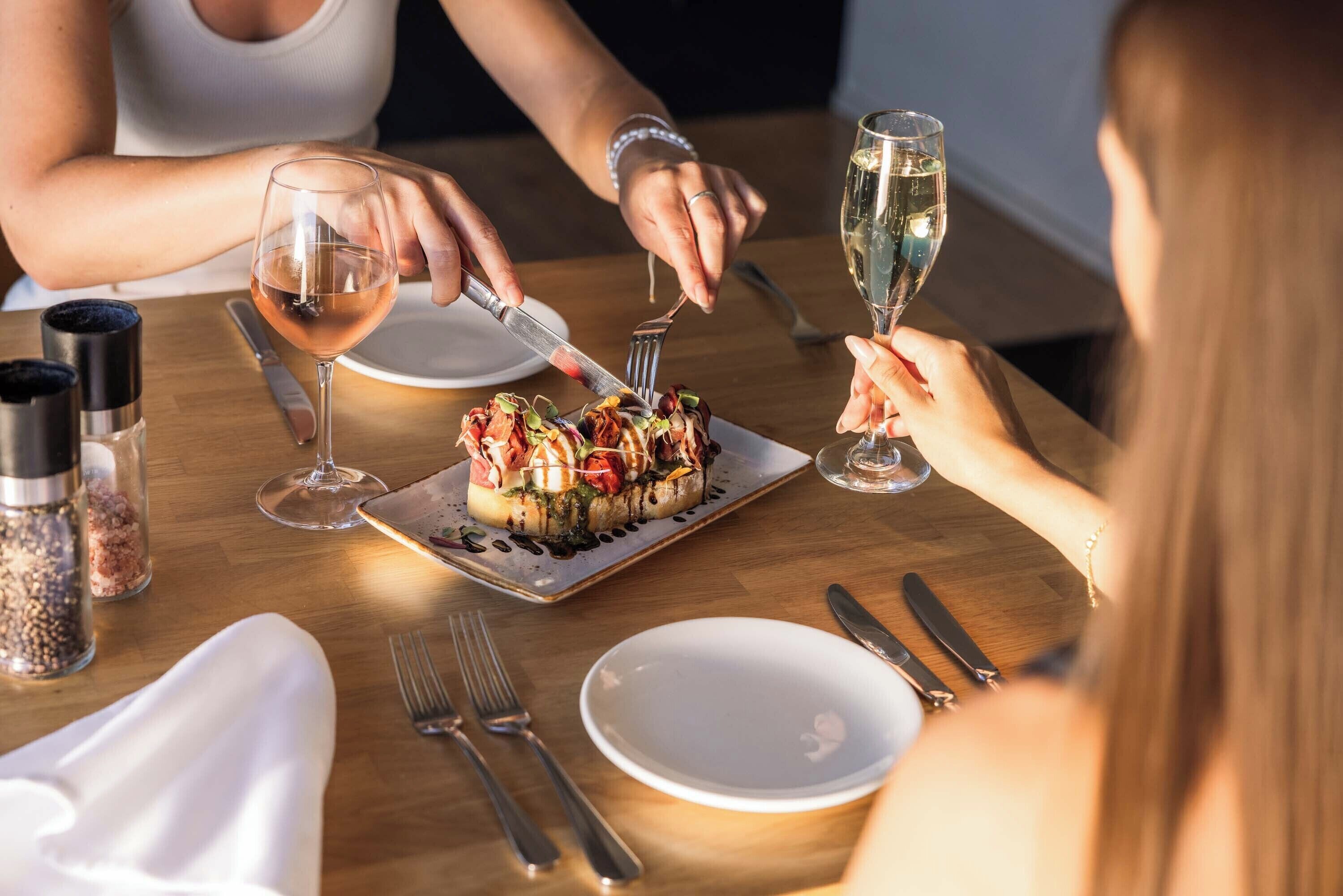 Una mesa de comedor con un plato de comida, copas de vino y cubiertos.