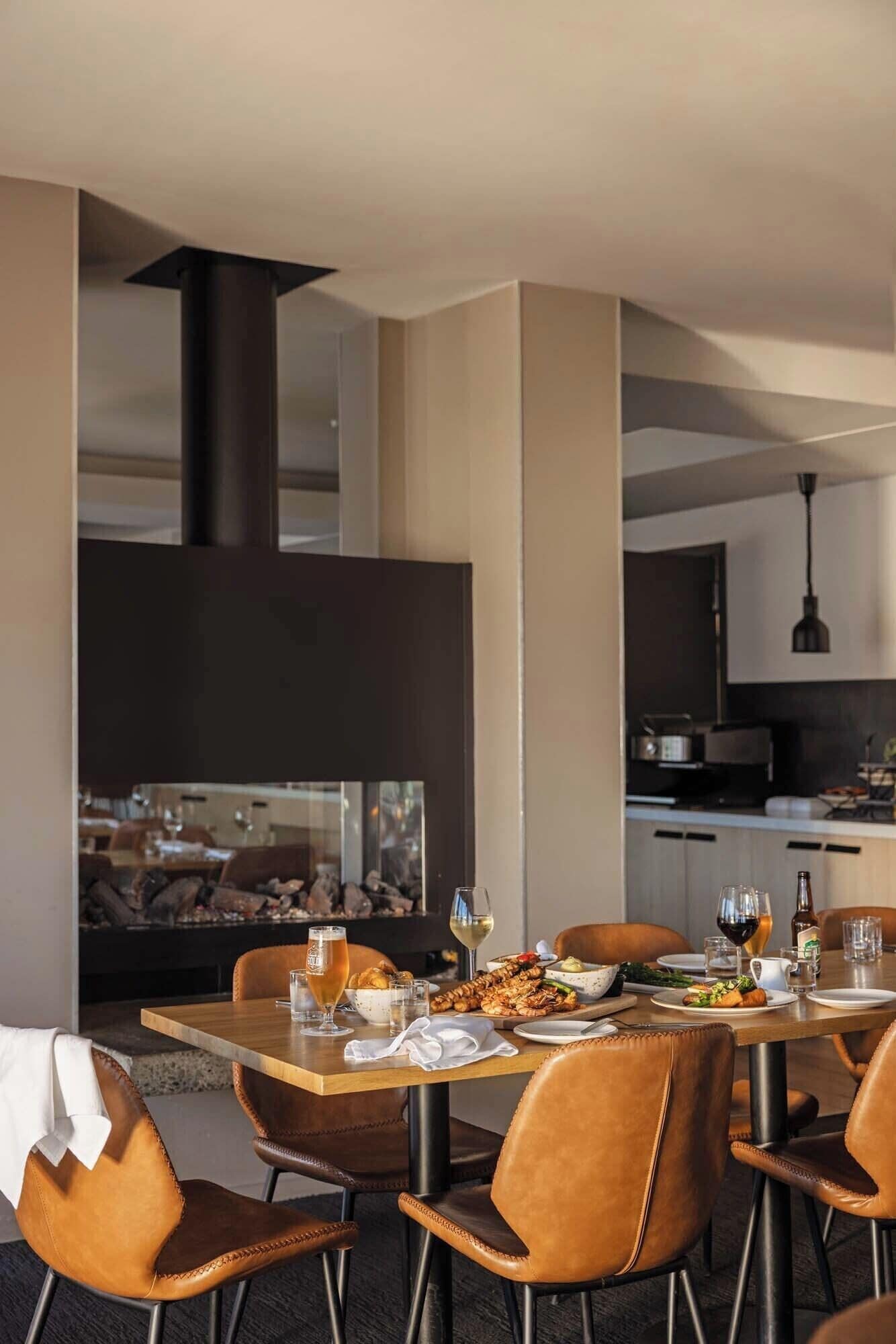 Een moderne eetruimte met een grote tafel, lederen stoelen en een uitzicht op een keuken en eetgedeelte op de achtergrond.