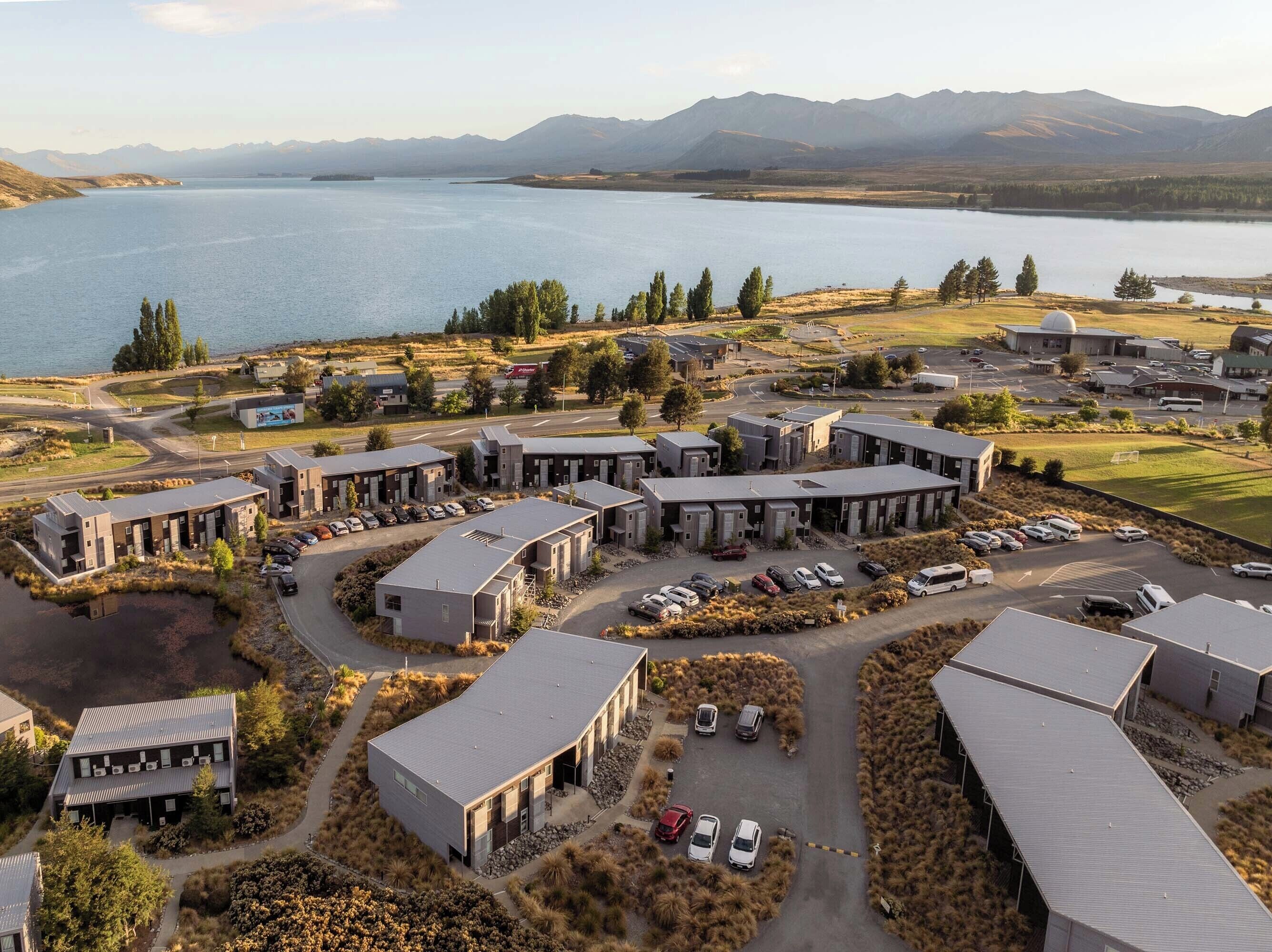 A modern building complex with multiple parking areas and a view of a lake and mountains in the background.