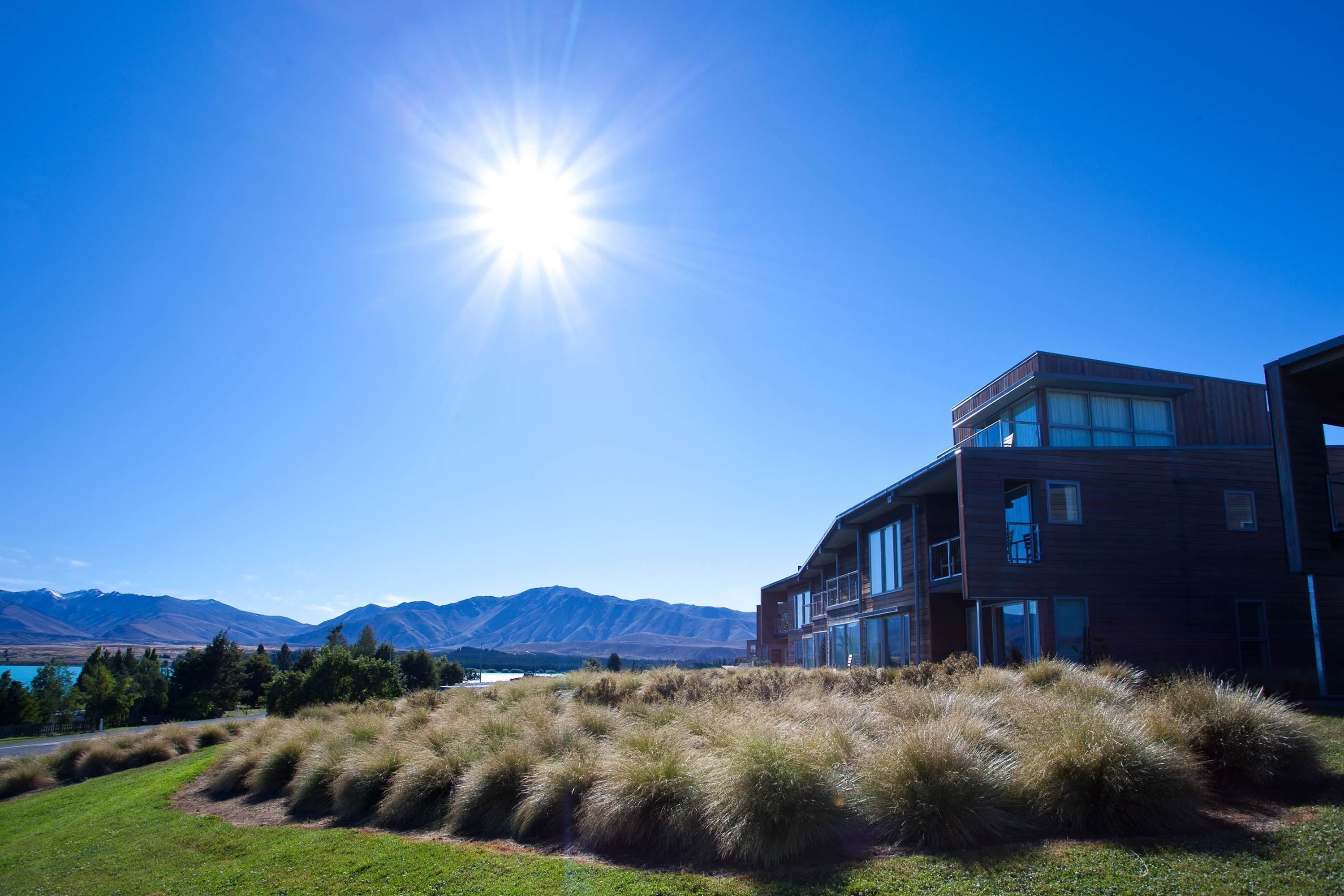 A modern building with a glass facade, surrounded by grassy areas and mountains in the background.
