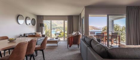 A modern hotel room with a dining area, a sofa, and a large window offering a view of the outdoors.