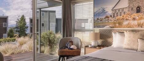A hotel room with a large bed, a chair, a nightstand, and a painting of a church.