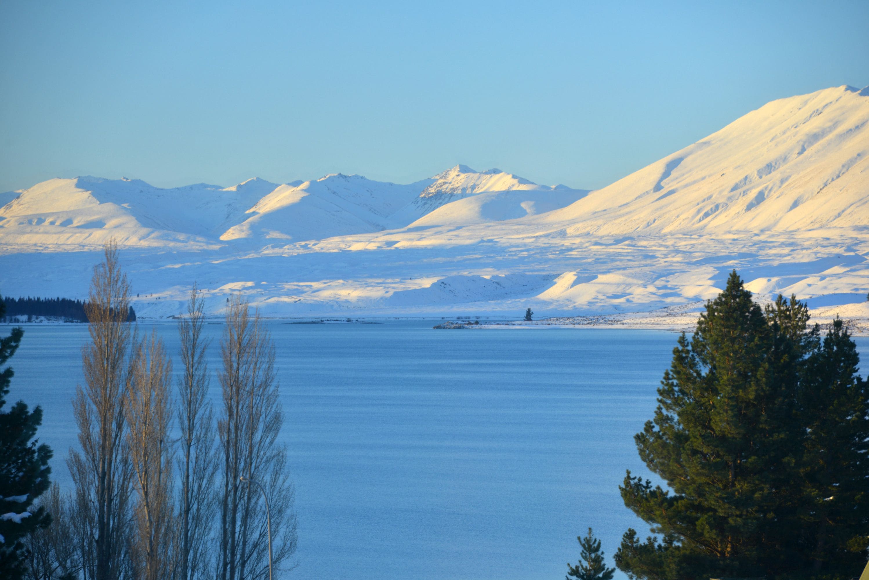 A panoramic view of a snow-covered landscape with mountains in the background and a body of water in the foreground.