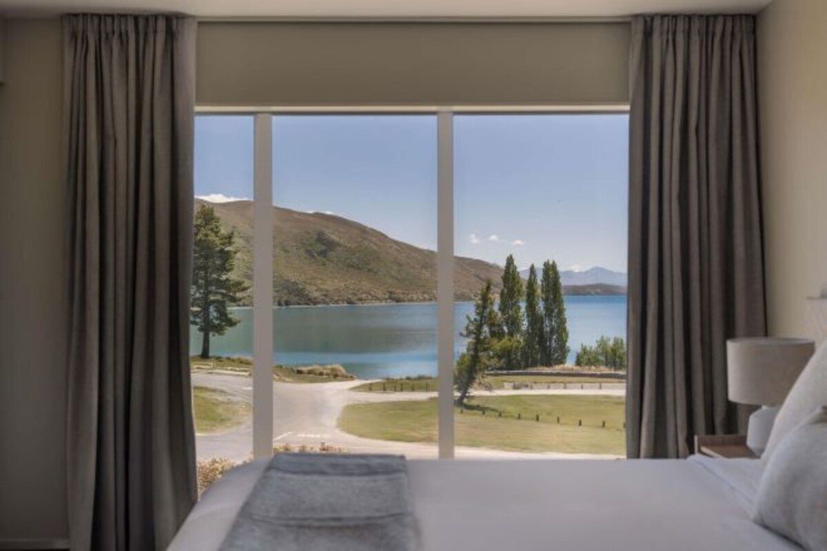 A hotel room with a large bed, a view of a lake, and curtains.