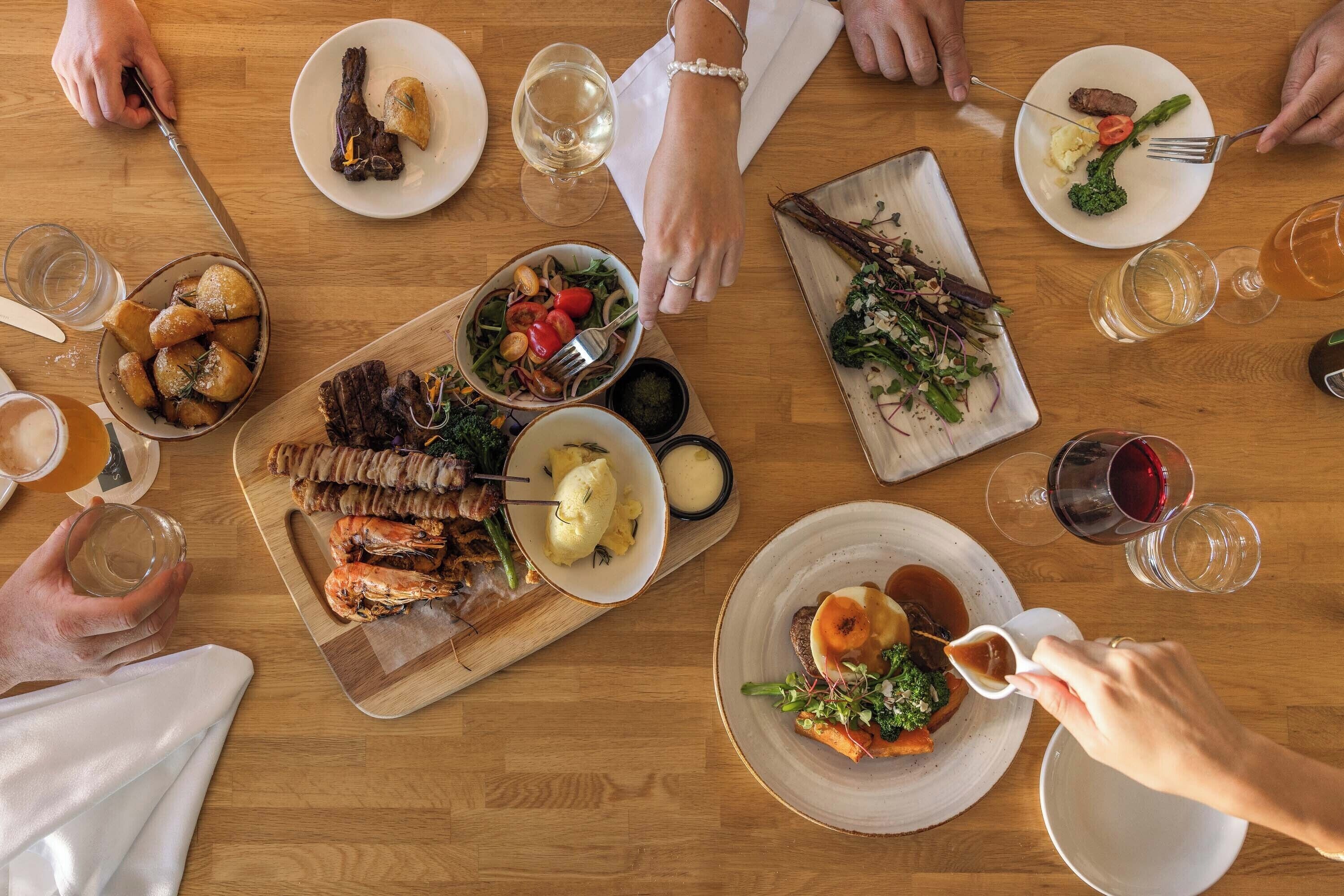 A wooden table with various dishes, including seafood, vegetables, and meat, along with glasses of wine.
